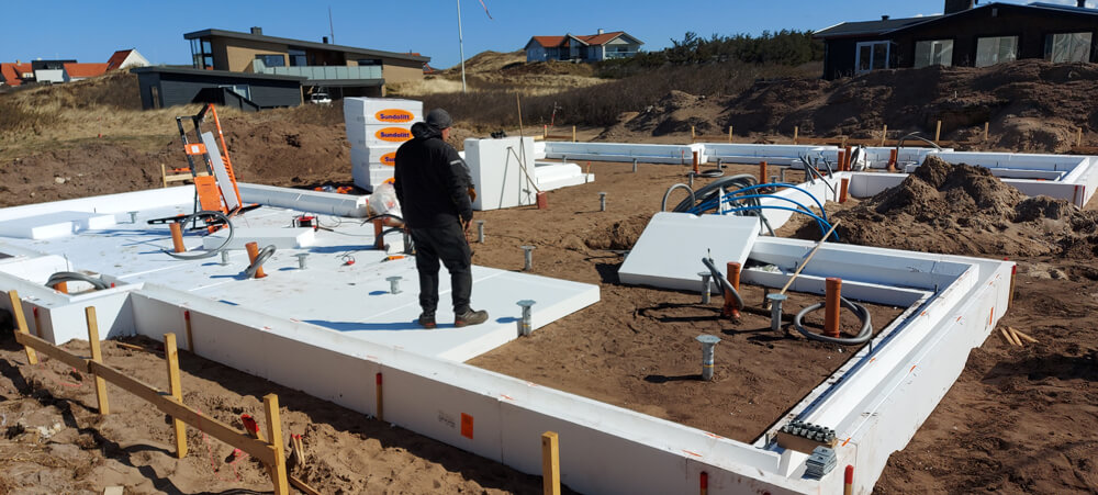 Foto fra byggeri på blødjord i Klitmøller. Hvide funderingsblokke lyser op på den brune jord.