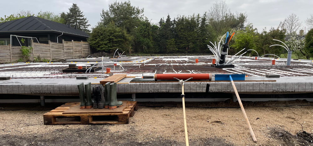 Støbeproces fundament på gammel mosegrund. Gummistøvler og redskaber står klar ved terrændæk med udlagt gulvvarme. Snart skal der støbes beton